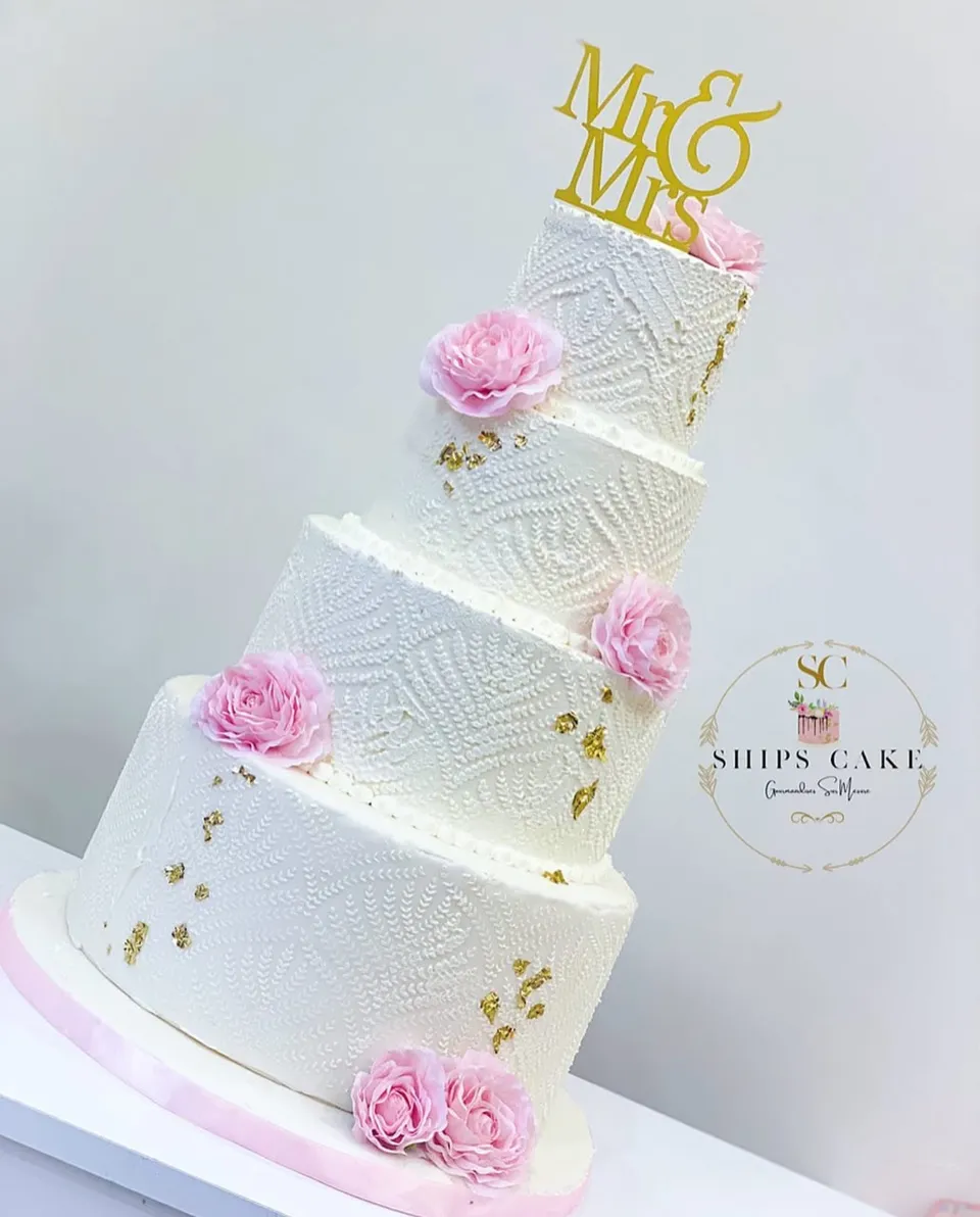 Pièce montée de mariage à quatre étages, glaçage blanc texturé, roses roses et éclats d'or