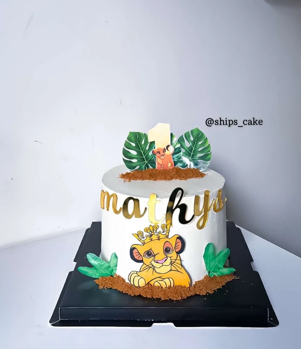 Gâteau blanc sur le thème du Roi Lion, avec un lionceau et des feuilles tropicales