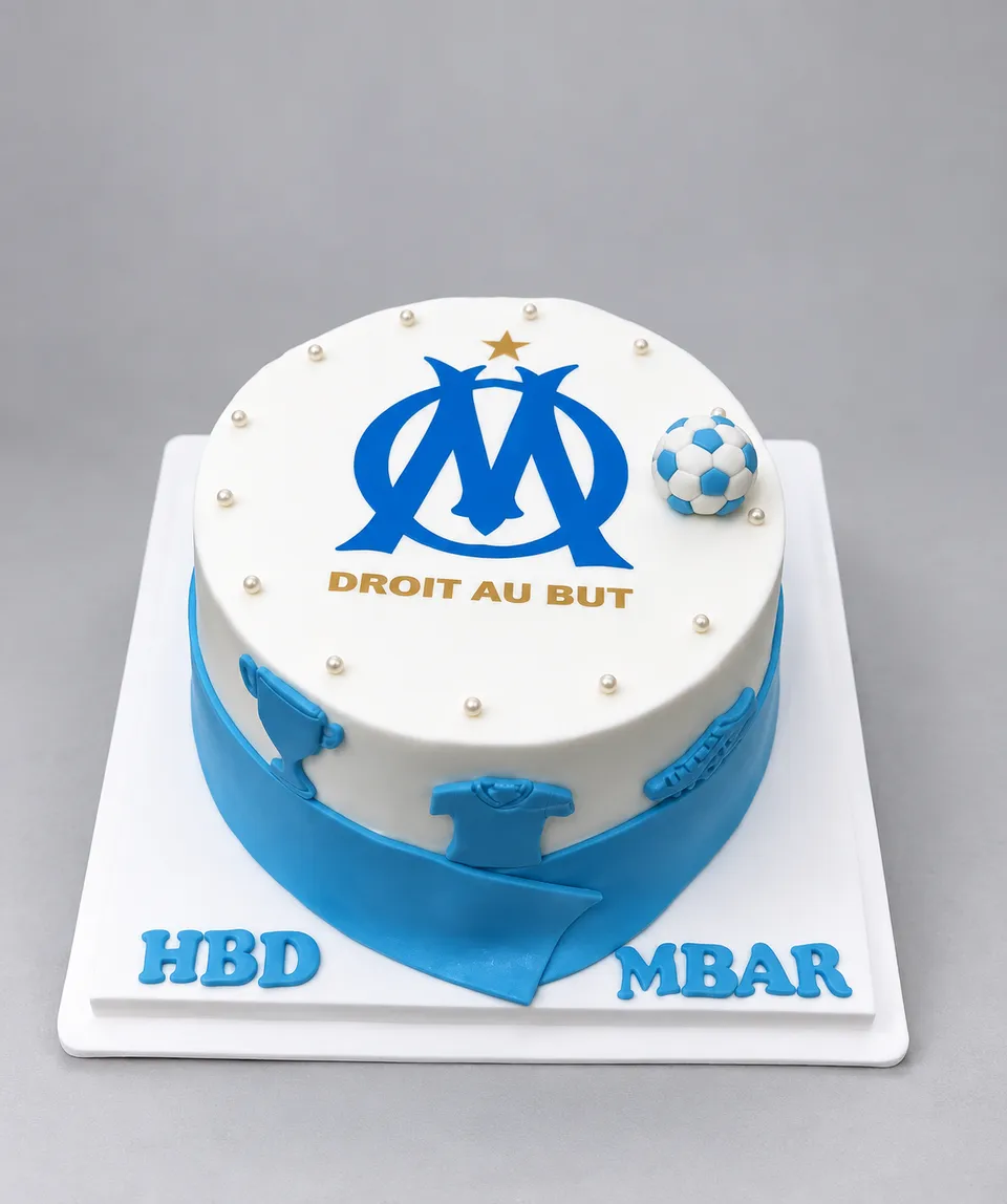 Gâteau blanc et bleu aux couleurs de l'Olympique de Marseille, avec un ballon et une écharpe en pâte à sucre